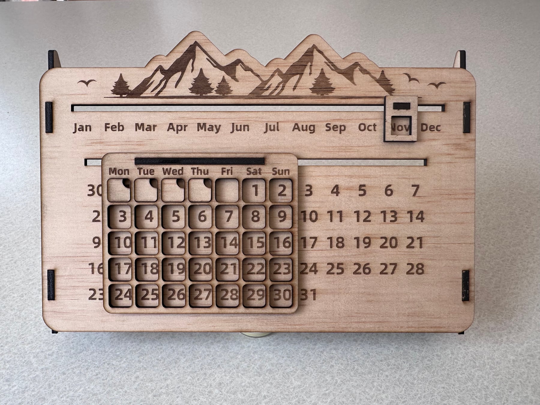 Wooden perpetual calendar with a mountain scene and movable month and date markers