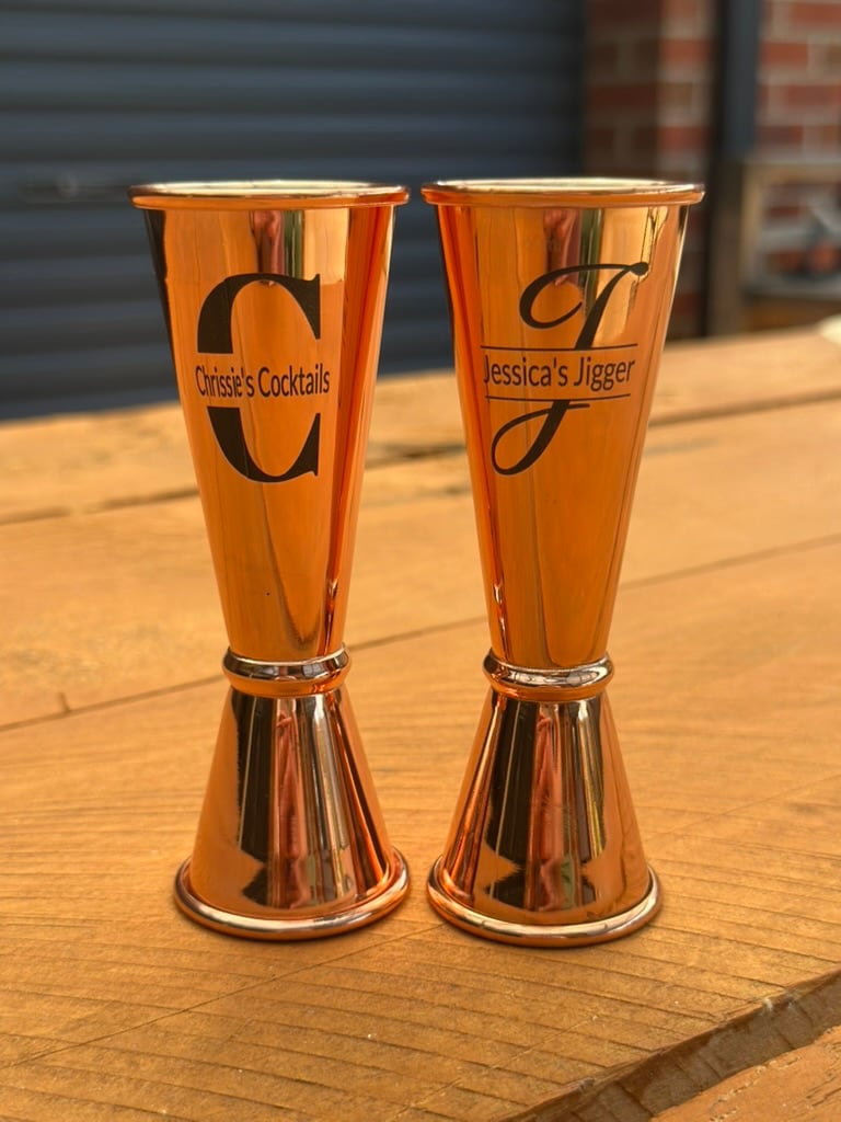 Two rose-gold cocktail jiggers engraved with names and initials